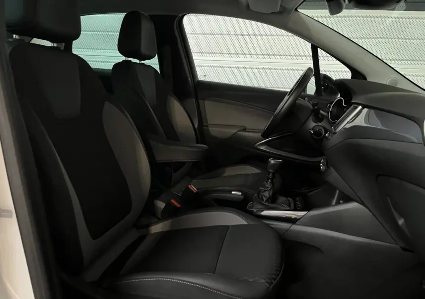 Vue intérieure côté conducteur de l'Opel Crossland X blanc, montrant les sièges noirs et la console centrale avec boîte manuelle.