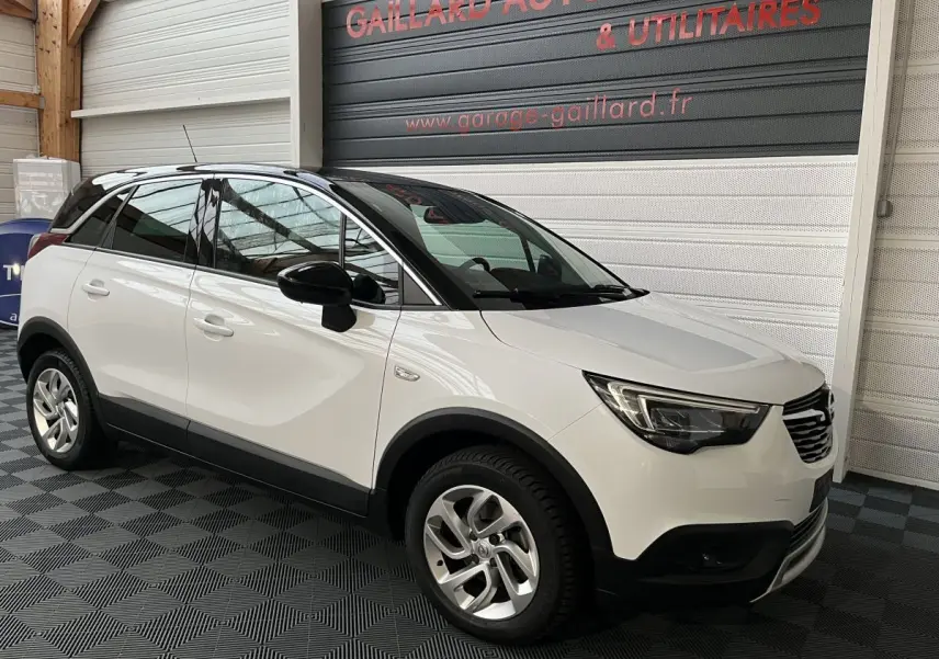 Vue 3/4 avant gauche d'un Opel Crossland X blanc avec toit noir, jantes alliage et détails noirs contrastants.