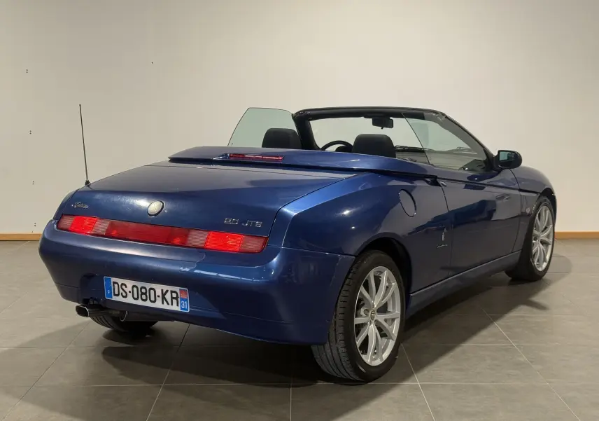 Vue 3/4 arrière droite d'un cabriolet Alfa Romeo Spider bleu 2006 avec capote ouverte et jantes argentées.