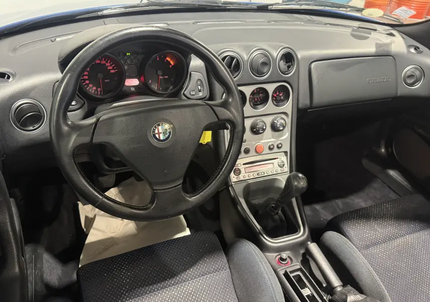 Vue intérieure de l'Alfa Romeo Spider 2.0 JTS 2006, volant cuir, tableau de bord noir et levier de vitesse manuel.