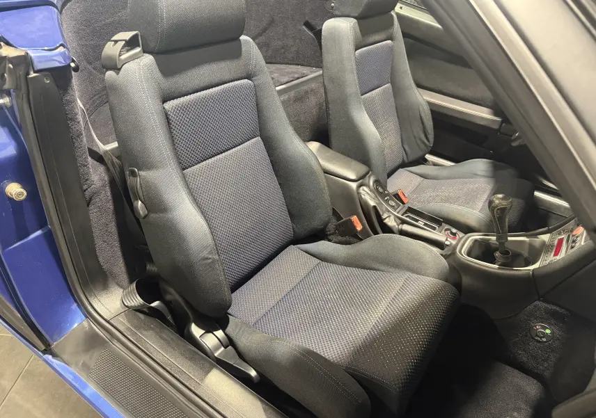 Vue intérieure côté conducteur de l'Alfa Romeo Spider bleu 2006, montrant les sièges sport et la boîte manuelle.