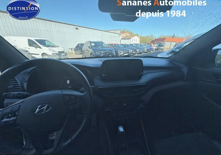 Vue intérieure du tableau de bord et volant du Hyundai Tucson gris foncé, avec écran tactile central et commandes au volant visibles.