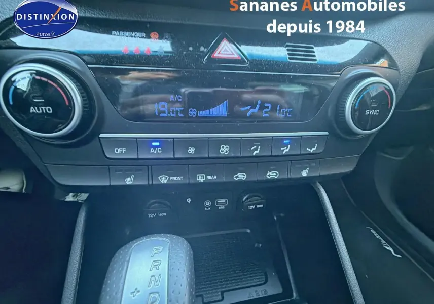 Vue rapprochée du tableau de bord et console centrale du Hyundai Tucson gris foncé, avec commandes climatisation et levier de boîte auto.