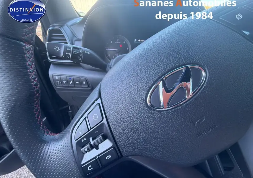 Gros plan sur le volant cuir perforé avec surpiqûres rouges du Hyundai Tucson 1.6 Hybrid gris foncé, tableau de bord partiel visible.