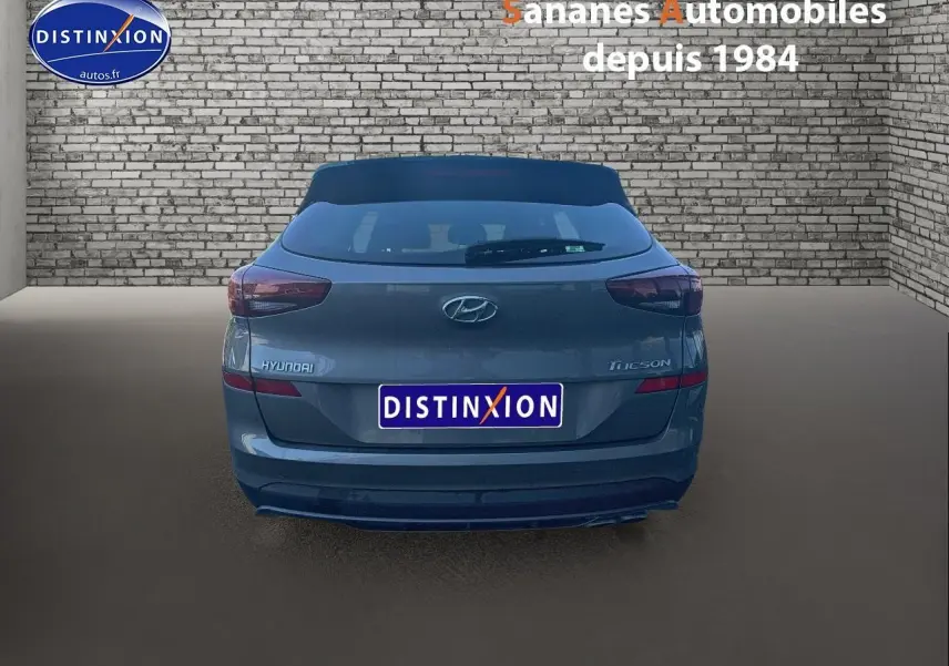 Vue arrière d'un Hyundai Tucson gris foncé 2020, avec logo et feux arrière visibles sur fond de mur en briques.