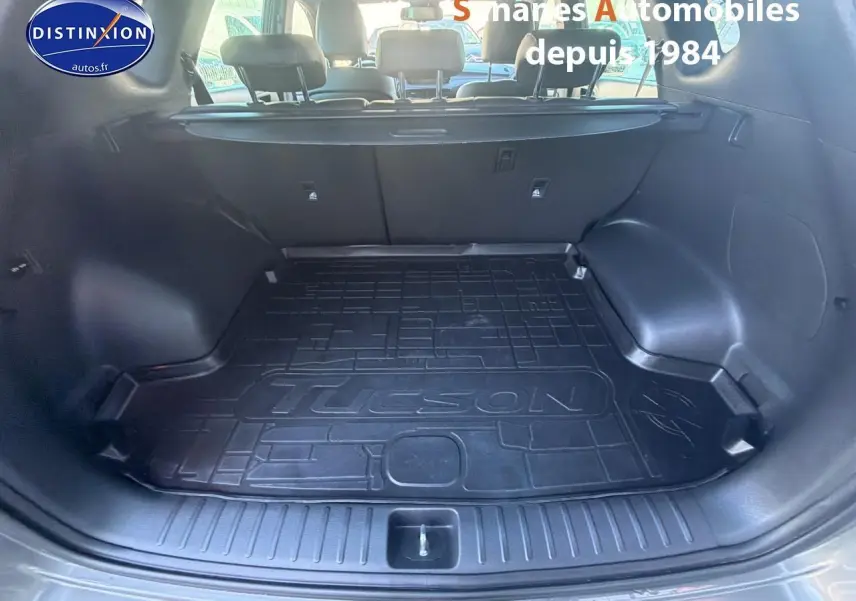 Coffre ouvert du Hyundai Tucson gris foncé, vue arrière montrant le tapis de coffre avec inscription Tucson.