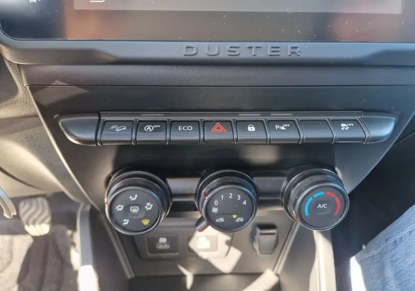 Gros plan sur la console centrale du Dacia Duster 2024, montrant les commandes de climatisation et les boutons fonctionnels noirs.