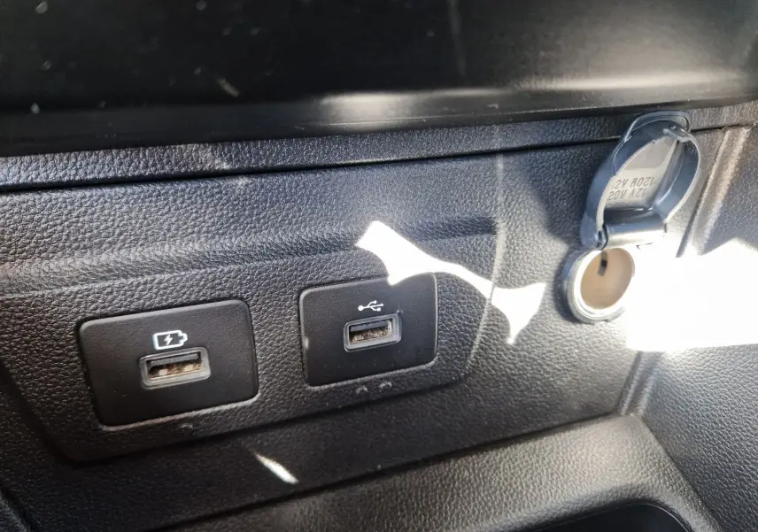 Gros plan sur les ports USB et prise 12V du tableau de bord noir du Dacia Duster blanc 2024.