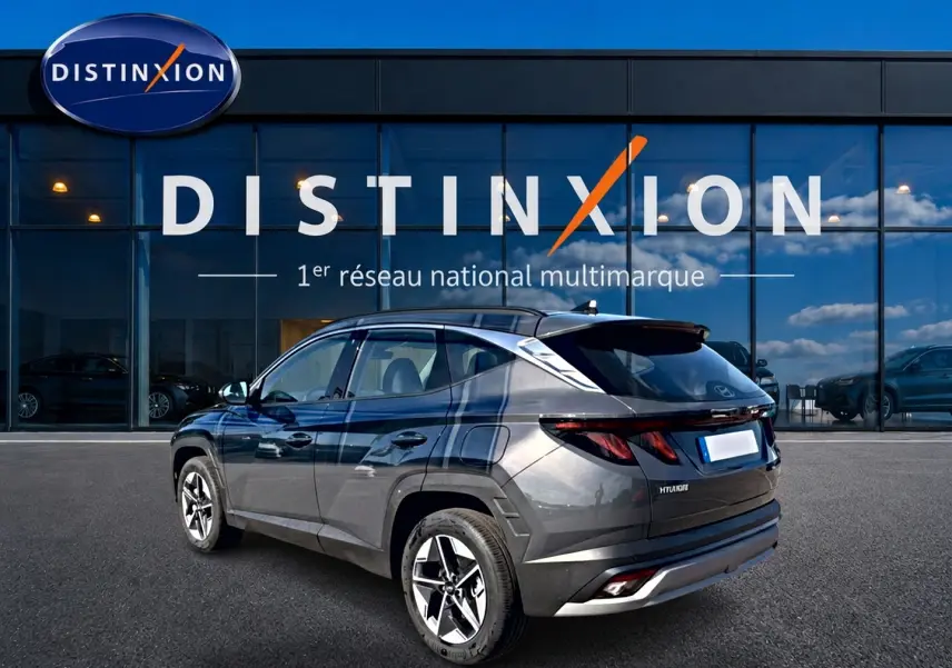 Hyundai Tucson 1.6 t-gdi 239 hybride gris ecotronic, vue 3/4 arrière droit devant un showroom Distinxion.