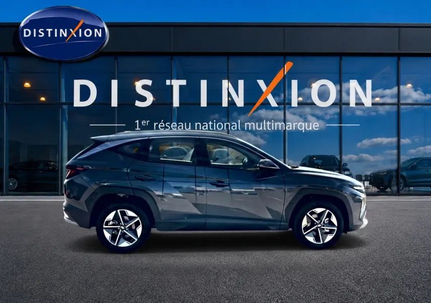 Vue de profil côté gauche d'un Hyundai Tucson gris ecotronic garé devant une vitrine avec logo Distinxion.