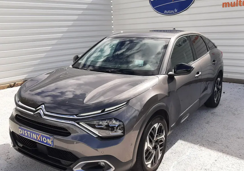 Citroën C4 gris 3/4 avant droit, avec phares LED et jantes alliage bicolores, stationné devant un mur blanc.