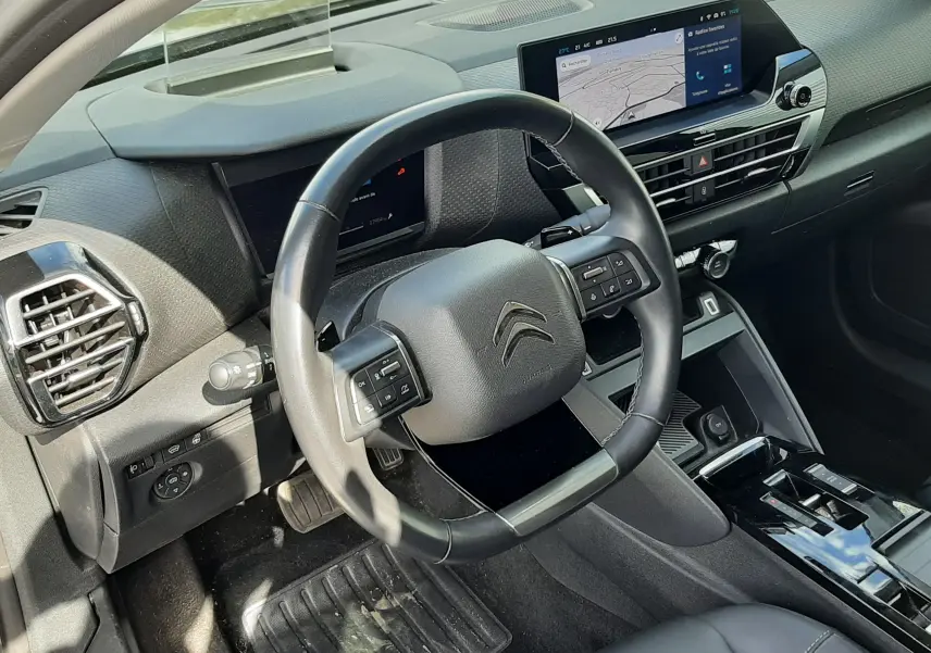Vue intérieure côté conducteur du tableau de bord gris et noir de la Citroën C4 1.2 PureTech 2024 avec écran tactile et volant multifonction.
