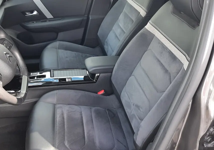 Vue intérieure côté conducteur de la Citroën C4 gris 2024, sièges en tissu et cuir noir avec bande grise, console centrale brillante.