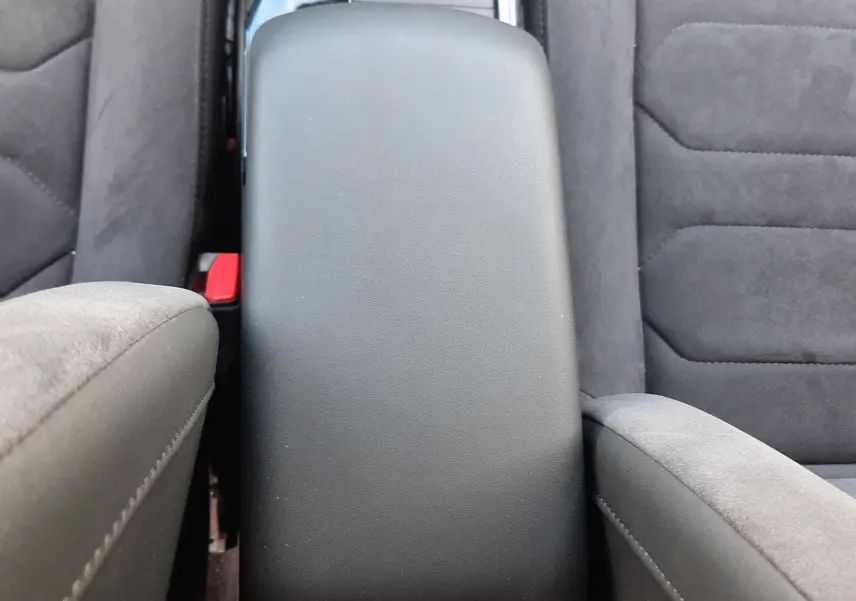 Vue plongeante sur l'accoudoir central noir et les sièges en tissu gris foncé de la Citroën C4 2024.