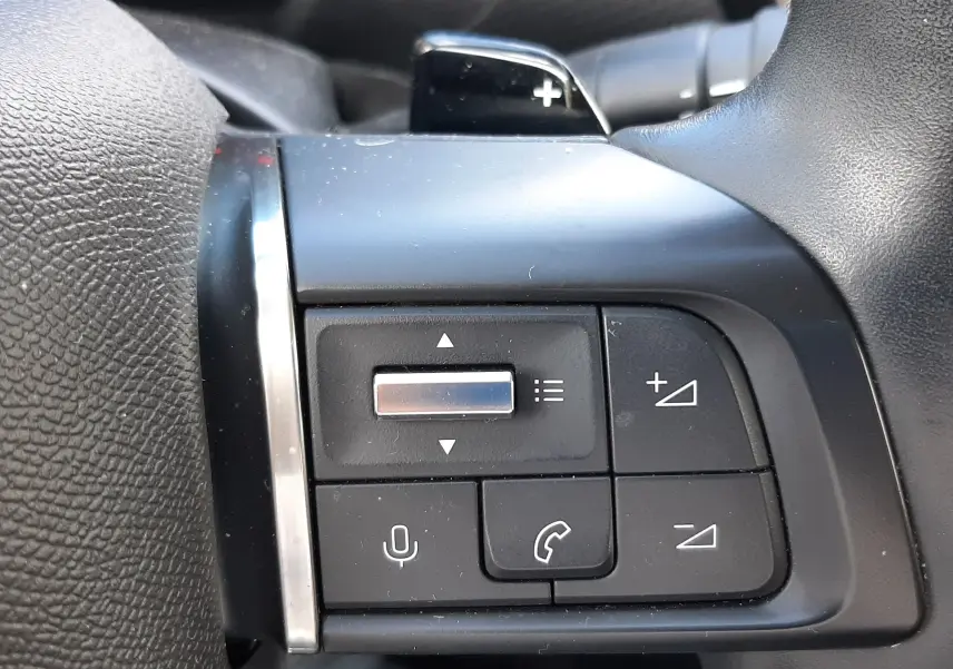 Gros plan sur les commandes multifonctions noires à gauche du volant du Citroën C4 gris 2024, avec palettes au volant.