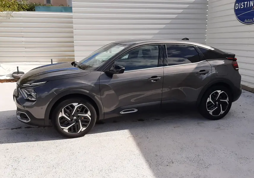 Profil côté gauche d'une Citroën C4 gris 2024, avec jantes bi-ton et vitres teintées, sur fond urbain clair.
