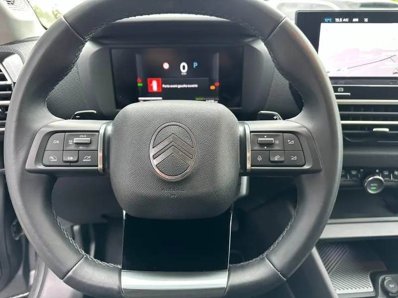 Vue rapprochée du volant noir du Citroën C4 X 2025 avec commandes intégrées et tableau de bord numérique en arrière-plan.