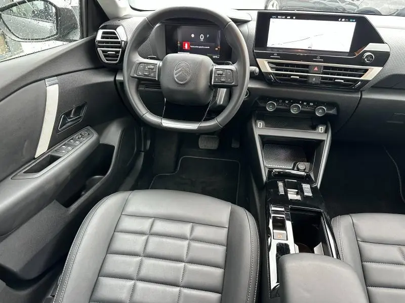 Vue intérieure de face du poste de conduite du Citroën C4 X gris Mercury 2025 avec volant multifonction et écran tactile central.