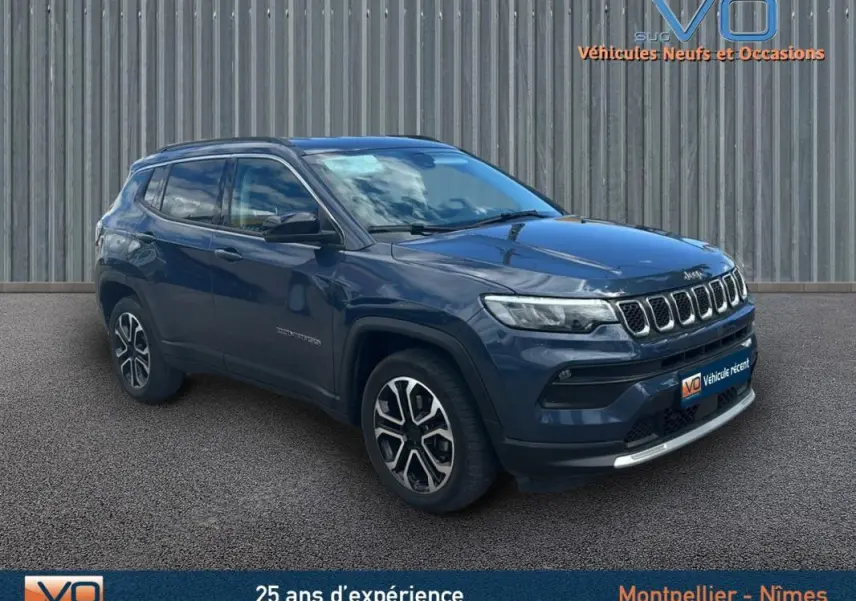 Jeep Compass bleu en 3/4 avant droit, avec barres de toit et jantes 18 pouces visibles sur fond neutre.