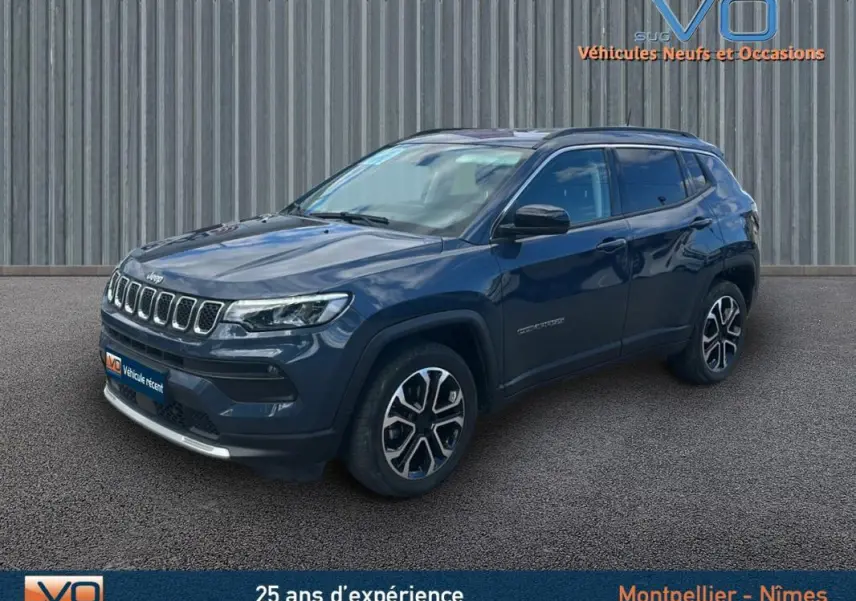 Jeep Compass bleu en 3/4 avant droit, avec barres de toit et jantes 18 pouces visibles sur fond urbain.