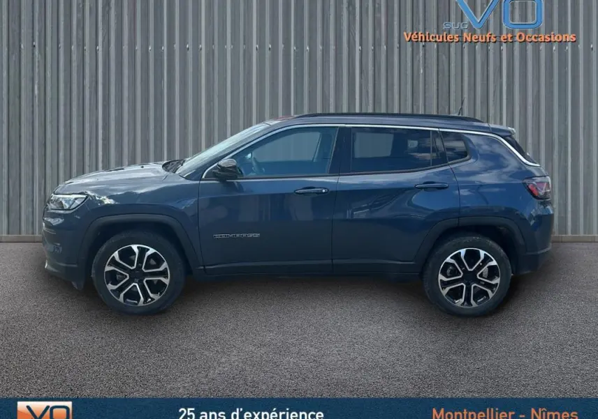 Profil côté gauche d'un Jeep Compass bleu 2023 avec jantes 18 pouces, barres de toit et vitres teintées.