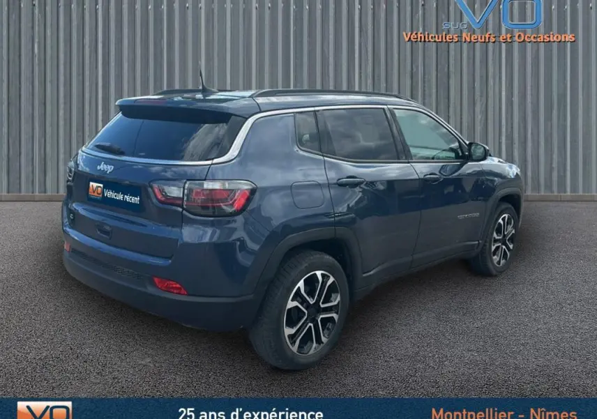 Vue 3/4 arrière droite d'un Jeep Compass bleu 2023 avec barres de toit et jantes 18 pouces visibles.