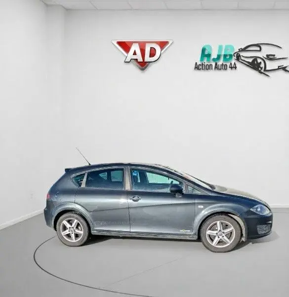 Vue de profil côté gauche d'une SEAT LEON II noire de 2013 avec jantes alu 16 pouces dans un showroom blanc.