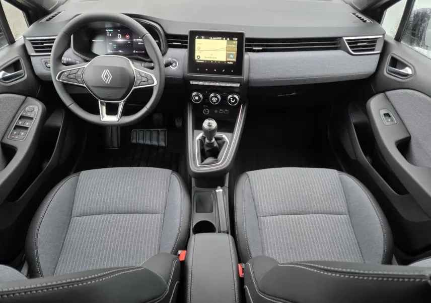 Vue intérieure avant de la Renault Clio 2025, tableau de bord gris avec volant multifonction et écran tactile central.