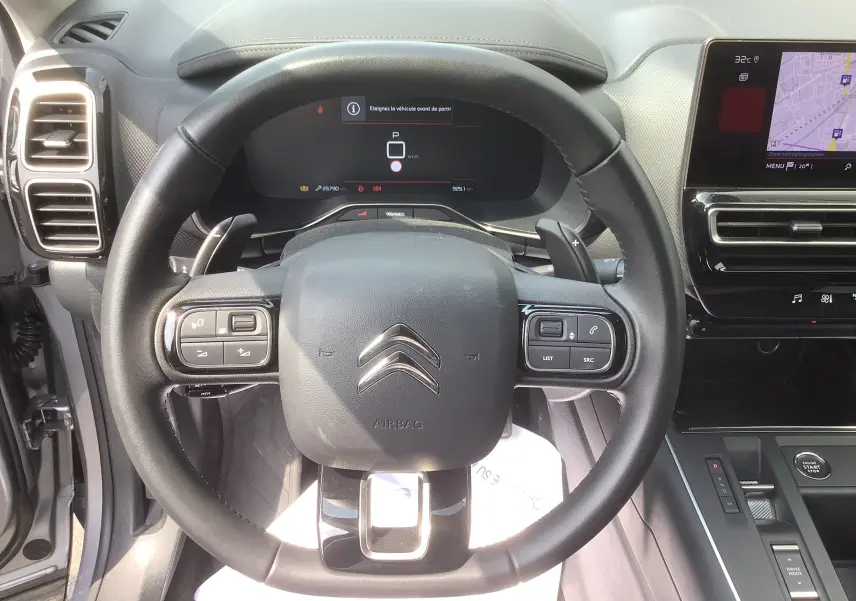 Vue intérieure centrée sur le volant noir du Citroën C5 Aircross Hybrid 2024 avec tableau de bord numérique et écran tactile.