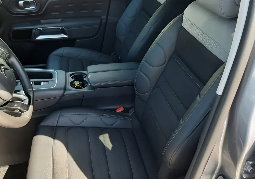 Vue intérieure côté conducteur du Citroën C5 Aircross Hybrid 2024 avec sièges en cuir noir et tissu gris, console centrale et porte gris acier.