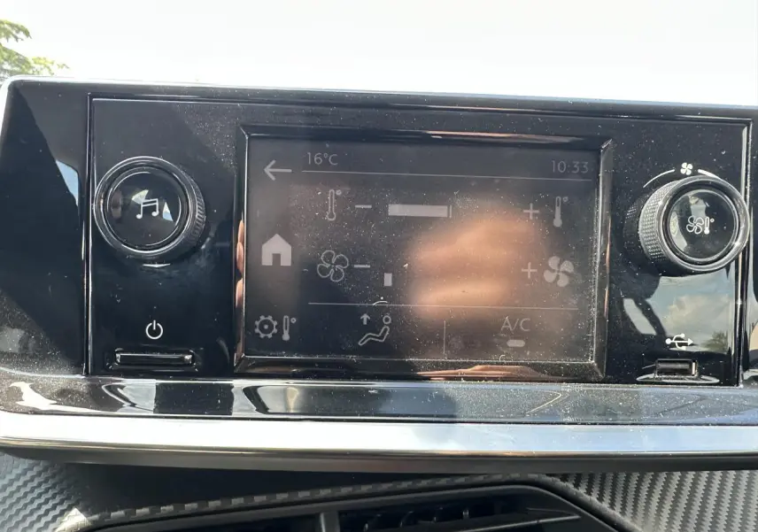 Vue rapprochée de l’écran tactile central noir de la Peugeot 208 blanche, affichant les réglages de climatisation.