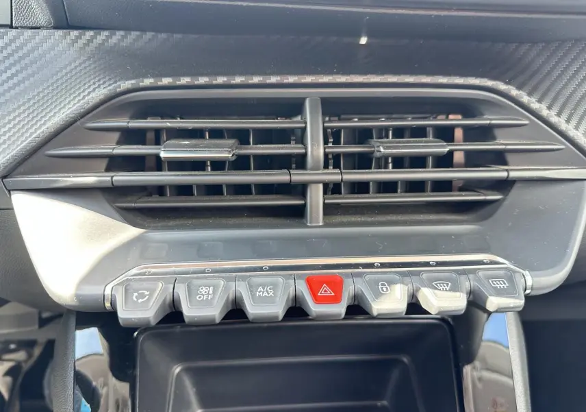 Gros plan sur la console centrale de la Peugeot 208 blanche, montrant les commandes d’air conditionné et les boutons fonctionnels.