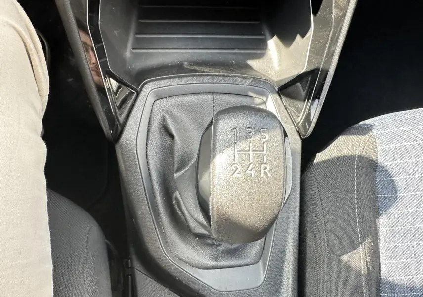 Gros plan sur le levier de vitesses manuel noir de la Peugeot 208 blanche, avec siège conducteur partiellement visible.