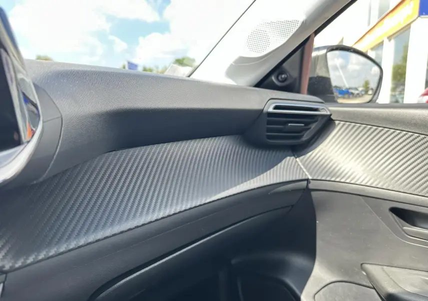 Détail de la garniture intérieure côté passager de la Peugeot 208 1.2i PT 75 blanche, avec effet carbone.