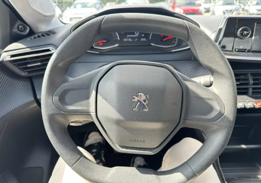Vue rapprochée du volant noir au design hexagonal du Peugeot 208 1.2i PT 75 Active 2021, intérieur moderne.