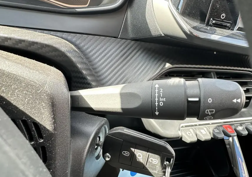 Gros plan sur la commande d’essuie-glace et la clé insérée dans le contact d’un Peugeot 208 blanc, intérieur avec finition carbone.