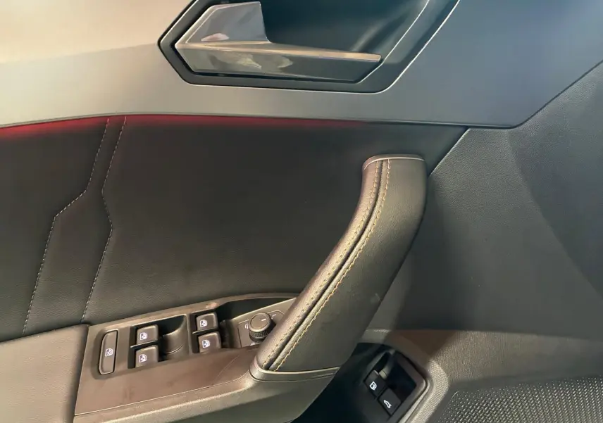 Vue intérieure du panneau de porte côté gauche d'une CUPRA Formentor 1.4 E-HYBRID 2024 avec commandes de vitres et poignée en cuir noir.