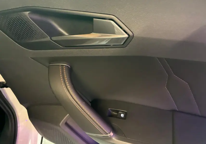 Poignée de porte intérieure côté gauche de la CUPRA Formentor gris, avec surpiqûres orange et bouton de verrouillage.