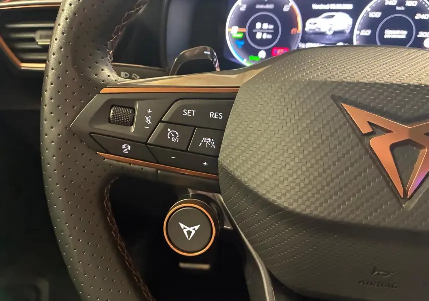Gros plan sur le volant perforé gris du CUPRA Formentor 1.4 E-HYBRID 2024 avec commandes intégrées et logo cuivré.