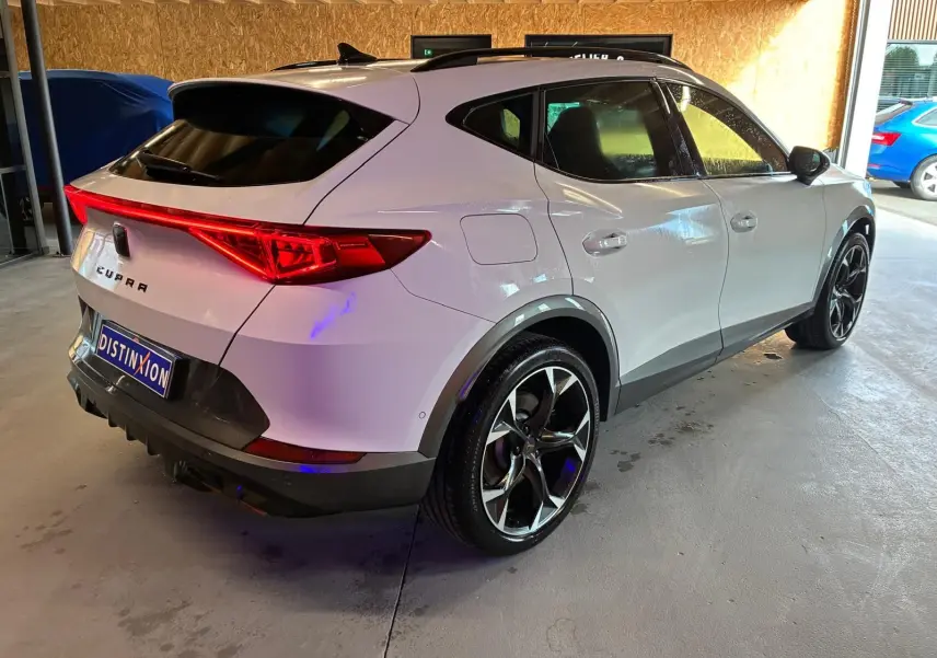 Vue 3/4 arrière droit d'un CUPRA Formentor gris avec feux arrière allumés et jantes noires bicolores.