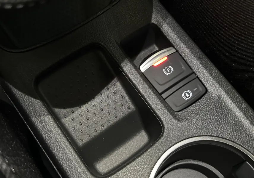 Gros plan sur la console centrale noire du Renault Captur II Ph.2, avec bouton de frein à main électronique allumé en rouge.