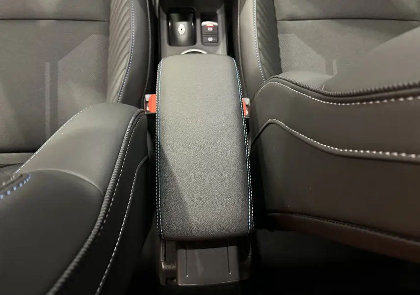 Vue rapprochée de l'accoudoir central en cuir noir avec surpiqûres bleues dans l'habitacle du Renault Captur blanc nacré.