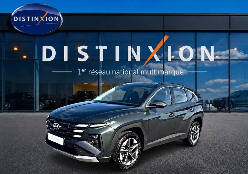 Hyundai Tucson 1.6 t-gdi 239 hybride vert en 3/4 avant droit devant un showroom Distinxion.