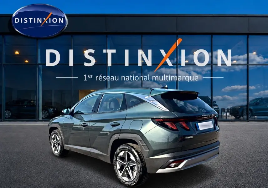 Vue 3/4 arrière gauche d'un Hyundai Tucson vert métallisé stationné devant une vitrine Distinxion.