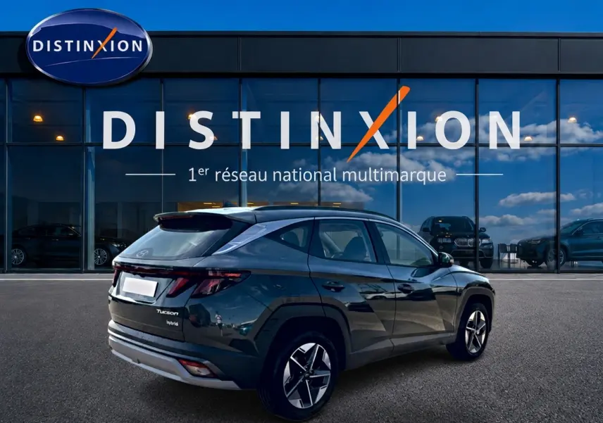 Vue 3/4 arrière droite d'un Hyundai Tucson hybride vert devant une vitrine Distinxion avec jantes alu 18 pouces.