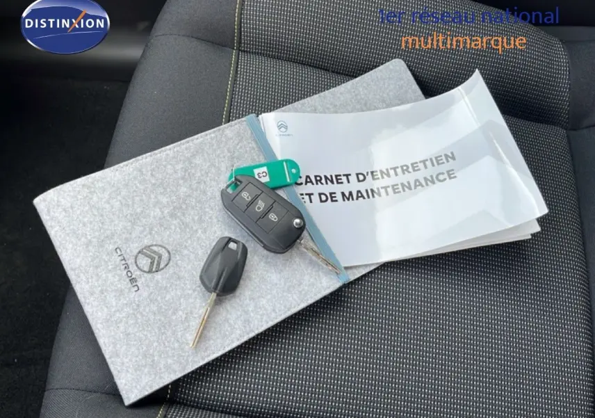 Vue rapprochée du carnet d’entretien Citroën et des clés posés sur un siège tissu gris noir de Citroën C3 2024.