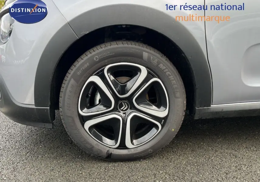 Gros plan sur la roue avant gauche d'une Citroën C3 2024 gris Artense métal avec jante alliage noire et argentée.
