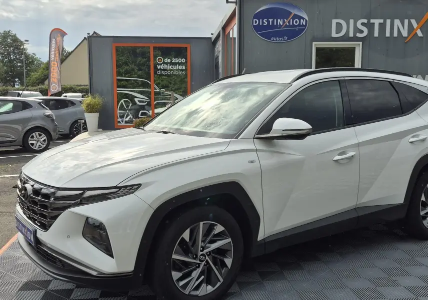 Hyundai Tucson blanc 2022 en 3/4 avant droit, avec calandre noire distinctive et jantes alliage bicolores.
