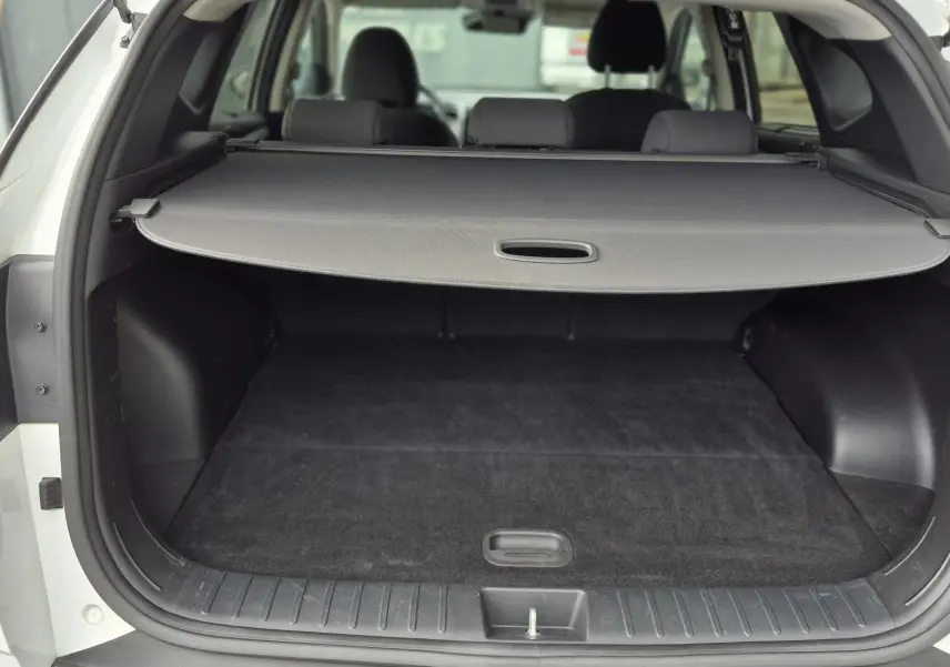 Vue arrière ouverte du coffre noir d’un Hyundai Tucson blanc 2022, avec cache-bagages déployé.