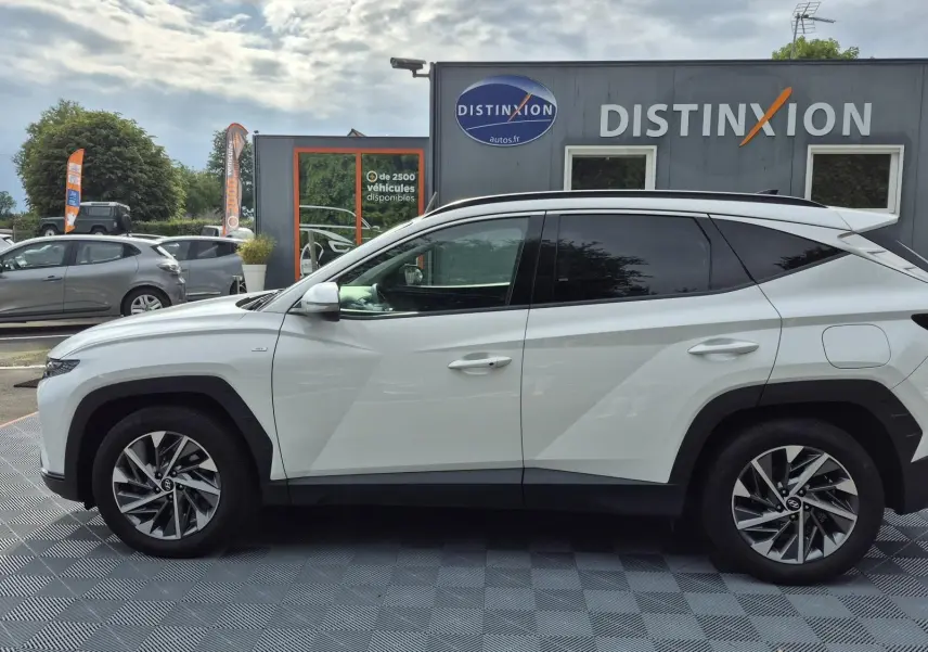 Vue de profil côté gauche d’un Hyundai Tucson blanc 2022 avec jantes alliage bicolores et vitres teintées.